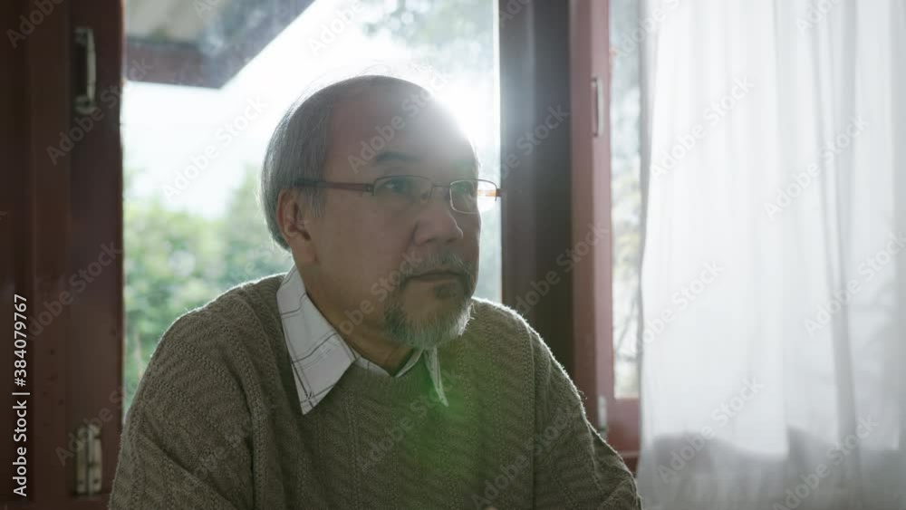 Close up : Sad old retired gray haired grandpa asian man sitting alone at table desk at window boring stay home self isolation quarantine feeling depress in problem mental health. Close up : Sad old retired gray haired grandpa asian man sitting alone at table desk at window boring stay home self isolation quarantine feeling depress in problem mental health.
