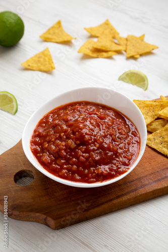 Homemade Tomato Salsa and Nachos on a rustic wooden board on a white wooden background, side view.