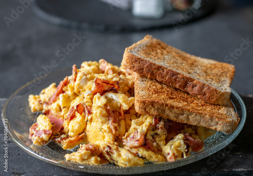 scrambles eggs with ham onions and whole wheat Toast on a glass plate