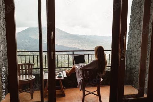 Fototapeta Back view of travel freelancer  woman working on laptop  with a mountain in the