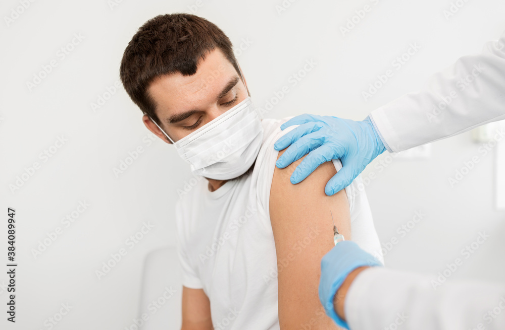 medicine, vaccination and healthcare concept - doctor or nurse's hands with syringe doing injection of vaccine to male patient wearing face protective medical mask for protection from virus disease medicine, vaccination and healthcare concept - doctor or nurse's hands with syringe doing injection of vaccine to male patient wearing face protective medical mask for protection from virus disease