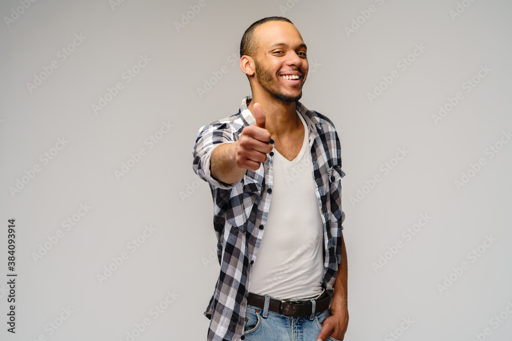 african-american young man wearing casual shirt and showing thumbs up over light grey background african-american young man wearing casual shirt and showing thumbs up over light grey background