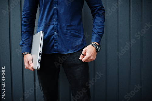 Close up photo of man hands with laptop against steel wall.