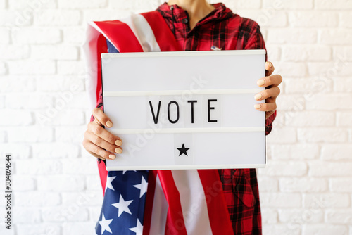 Photos Woman with american flag holding lightbox with the word Vote on white brick back