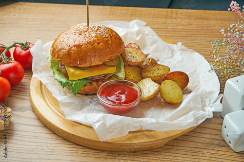 Juicy burger with beef, melted cheese, cucumber and young potato garnish on parchment. American fast food