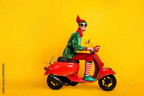 Profile side view of his he nice attractive cheerful cheery funny guy elf riding moped having fun enjoying leisure winter season isolated over bright vivid shine vibrant yellow color background © deagreez