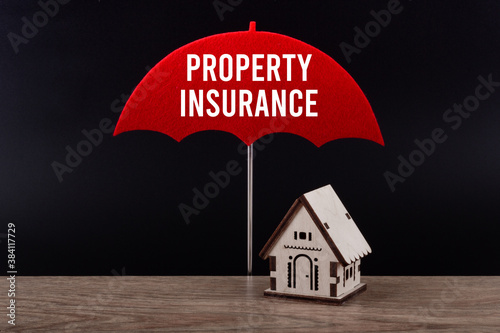 Concept of house insurance. Wooden house under red umbrella with text Property insurance.