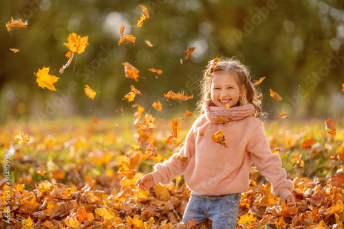 Happy little girl throws autumn leaves and laughs outdoors in the autumn Park  on a Sunny day. The child is happy about the onset of autumn and plays with colorful leaves.