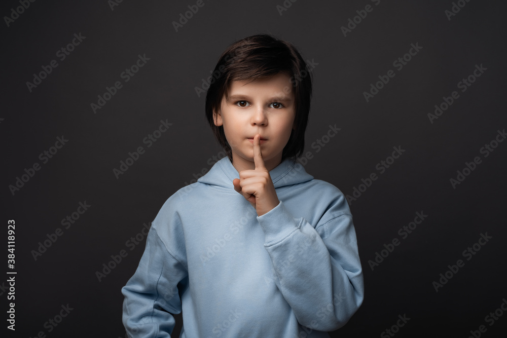 Portrait of Cute boy holding index finger on lips. Silence and secret concept. Studio shot, gray background Portrait of Cute boy holding index finger on lips. Silence and secret concept. Studio shot, gray background