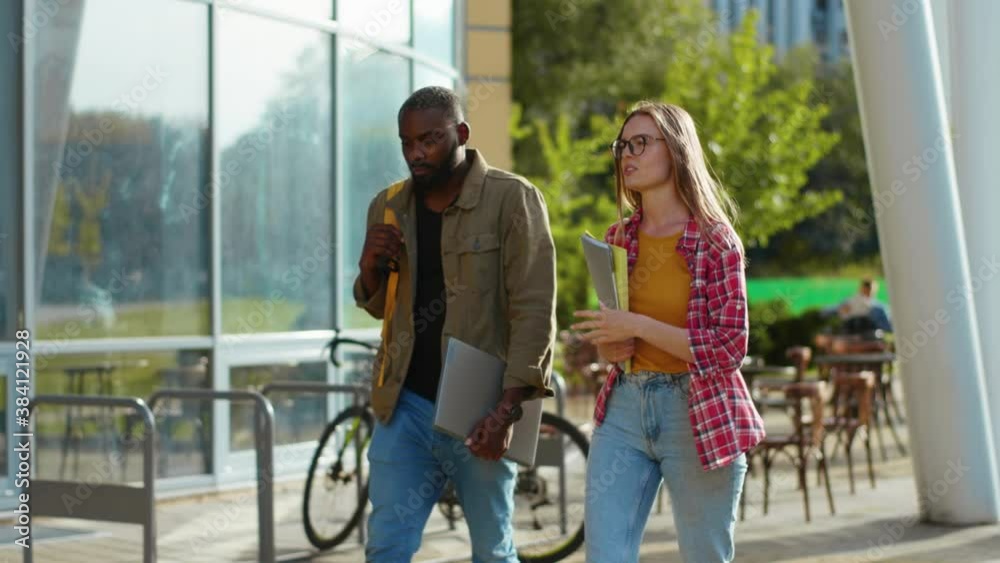 Diverse attractive modern couple of young students walking near campus building communicating about classes. Mixed-race people. Education and friendship. Diverse attractive modern couple of young students walking near campus building communicating about classes. Mixed-race people. Education and friendship.