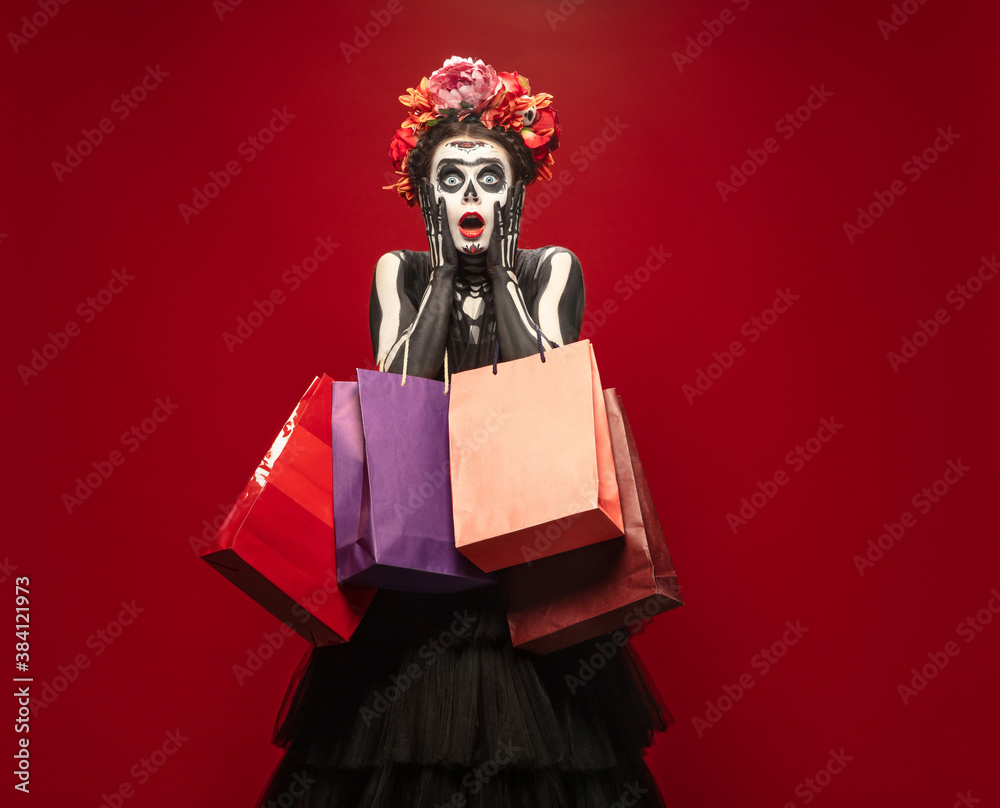 Shopping. Young girl like Santa Muerte Saint death or Sugar skull with bright make-up. Portrait isolated on red studio background with copyspace. Celebrating Halloween or Day of the dead. Black friday