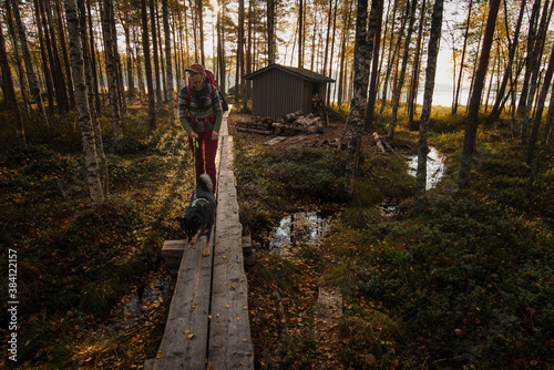 Woman and dog alone on path in autumn forest with backlit sunlight