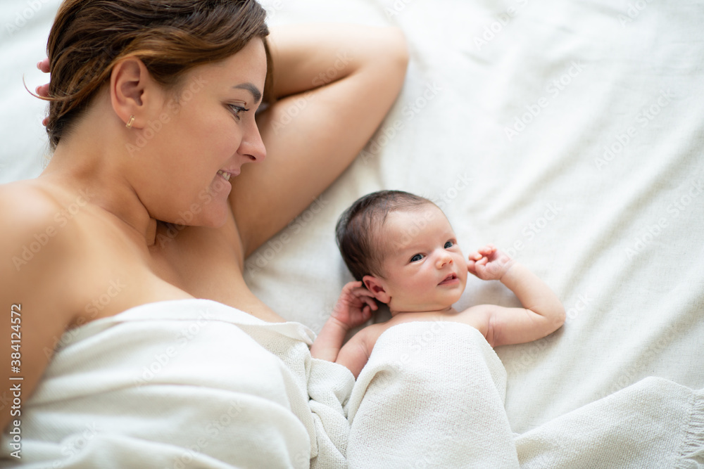 Mother lying in bed with her newborn daughter at home, takes care about baby. Family values, mothercare Mother lying in bed with her newborn daughter at home, takes care about baby. Family values, mothercare