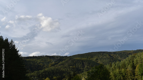 Wolken und Sonne wechseln sich ab über Hügelland mit Wald