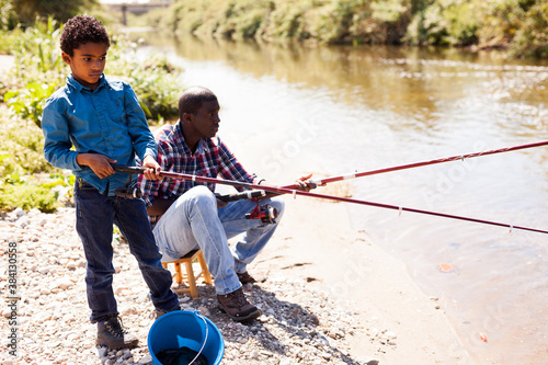 Portrait of fishermen - African boy and his father fishing with rods on river
