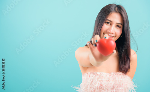 Portrait asian beautiful woman smiling her Stick out red heart on hand and her looking to camera on blue background, with copy space for text
