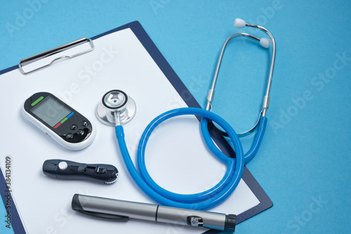 clipboard with white blank sheets of paper, stethoscope, glucose meter, lancet and syringe pen with insulin on blue background, daibet day concept, diabetes diagnostics