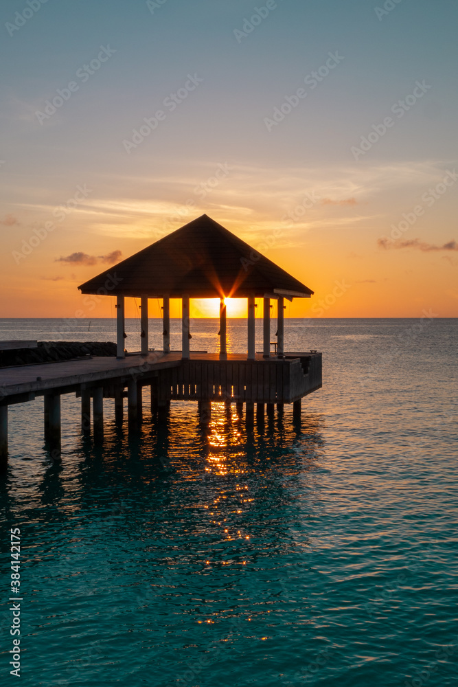 Sun light goes through building on water of Indian ocean during sun set on Maldive islands
