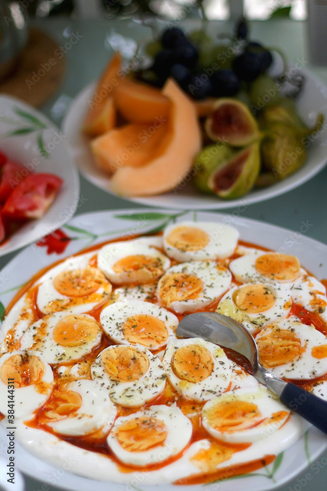 Boiled eggs with yoghurt sauce, tomato salda and various fruit on the breakfast table. Selective focus.