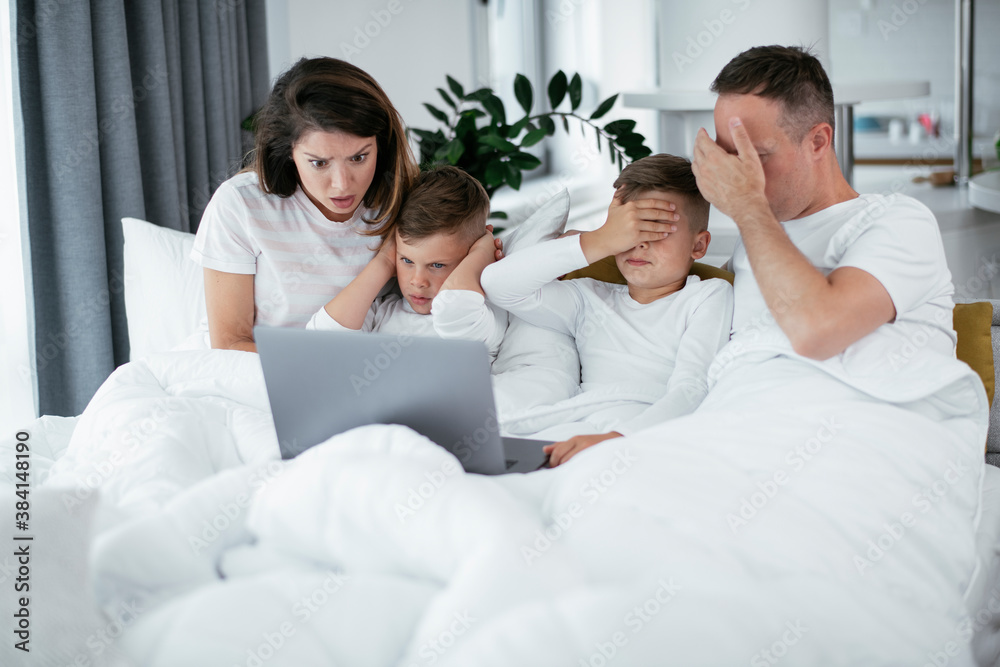 Beautiful parents with kids enjoying at home. Young family watching movie on lap top