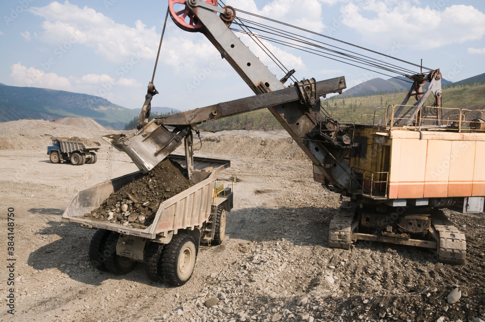 Excavator loads mountain soil into the body of a mining dump truck and then transports the load. Extraction of minerals in the mountainous region of Eastern Siberia Excavator loads mountain soil into the body of a mining dump truck and then transports the load. Extraction of minerals in the mountainous region of Eastern Siberia