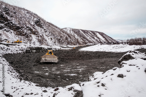 Fototapeta Naklejka Na Ścianę i Meble -  The bulldozer harrows the mountain soil, and then removes the top layer with an industrial bucket. Extraction of minerals in mountainous areas, in Siberia (gold mining)