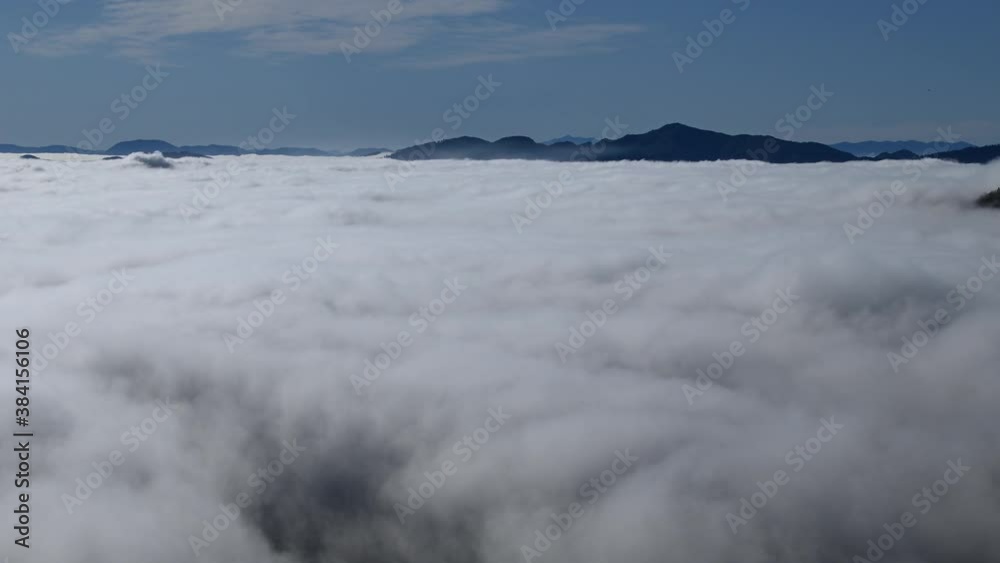 Time lapse low altitude inversion clouds rolling in valley. Elevated view above the fog. Hills and mountains in the distance. Zoom out Time lapse low altitude inversion clouds rolling in valley. Elevated view above the fog. Hills and mountains in the distance. Zoom out