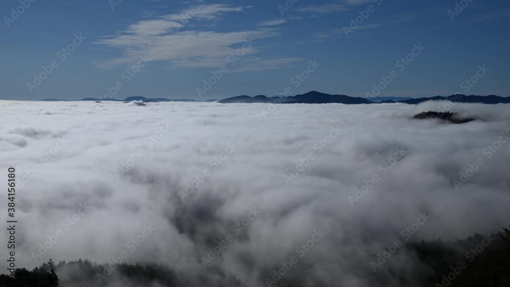 Time lapse low altitude inversion clouds rolling in valley. Elevated view above the fog. Hills and mountains in the distance. Static shot, wide angle