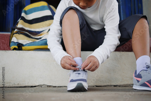 Asian schoolboy in casual clothing tying shoelaces on sneakers getting ready for school or traveling.