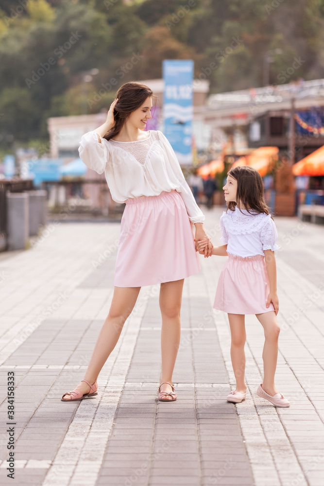 Young cheerful mom with daughter on a walk in european city. Little girl smiling and having fun. Summer portrait with space for text.