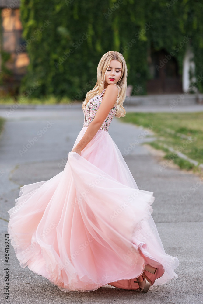 Blonde woman with make up in evening dress at park. The skirt of her dress fly on a wind. Sensual fashion portrait with a sunset light Blonde woman with make up in evening dress at park. The skirt of her dress fly on a wind. Sensual fashion portrait with a sunset light