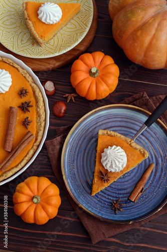 pumpkin pie with cinnamon and cream in a cut. Autumn table setting for Thanksgiving and Halloween. pumpkins, cinnamon sticks, plates, wooden background 