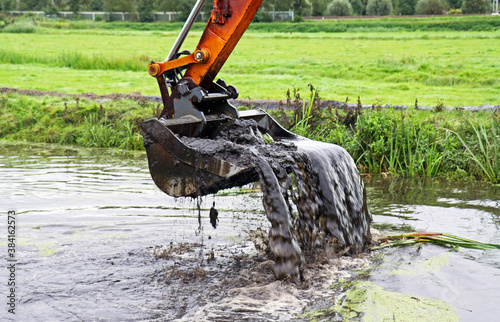 Dredging: crane with backhoe takes a scoop of sediment from a canal photo