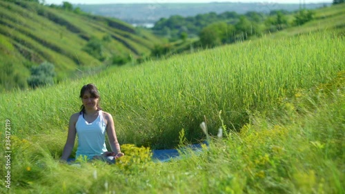 Young woman doing yoga in green summer meadow