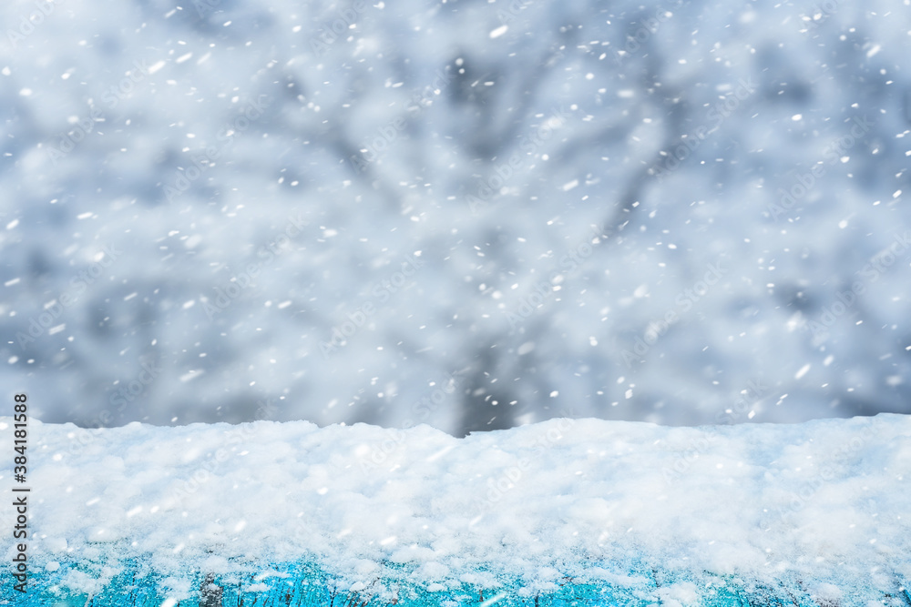 Snow-covered wooden table on blurred background during snowfall, winter background