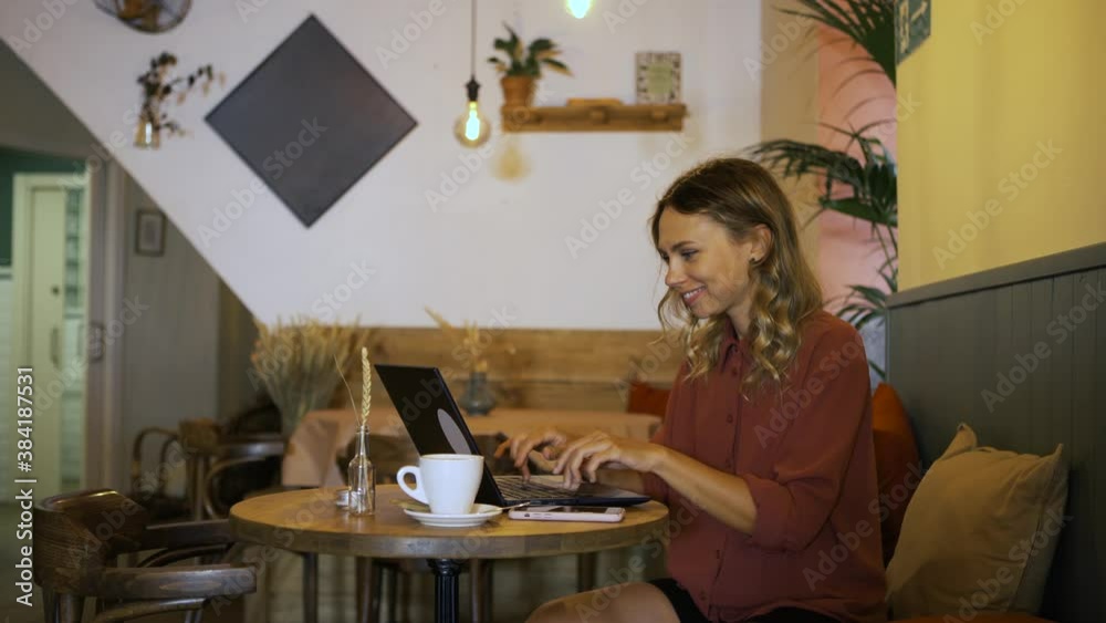 Smiling female freelance working with laptop in a coffee shop. Attractive business woman being productive outside the office. Hands typing fast. Smiling female freelance working with laptop in a coffee shop. Attractive business woman being productive outside the office. Hands typing fast.