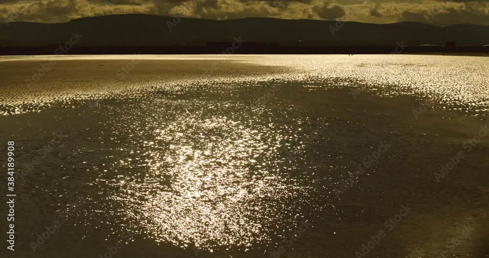 Sunlight reflecting off a shallow pool on a beach with mountains in the background