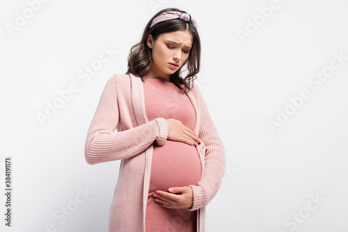 Fotografia worried pregnant woman in headband touching and looking at belly on white