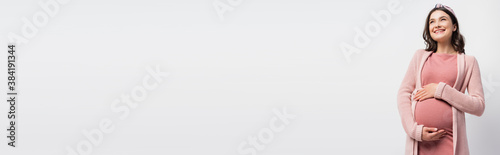 horizontal image of pregnant woman in cardigan and headband touching belly isolated on white