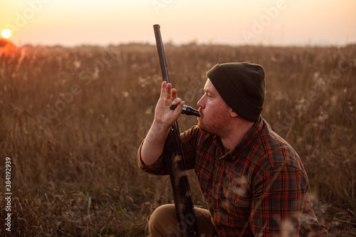 Photographie Young red bearded hunter  sitting it grass and blowing at hunter's whistle - pho