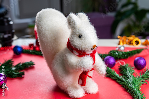 Christmas toy white squirrel on a red background in a red scarf with Christmas entourage