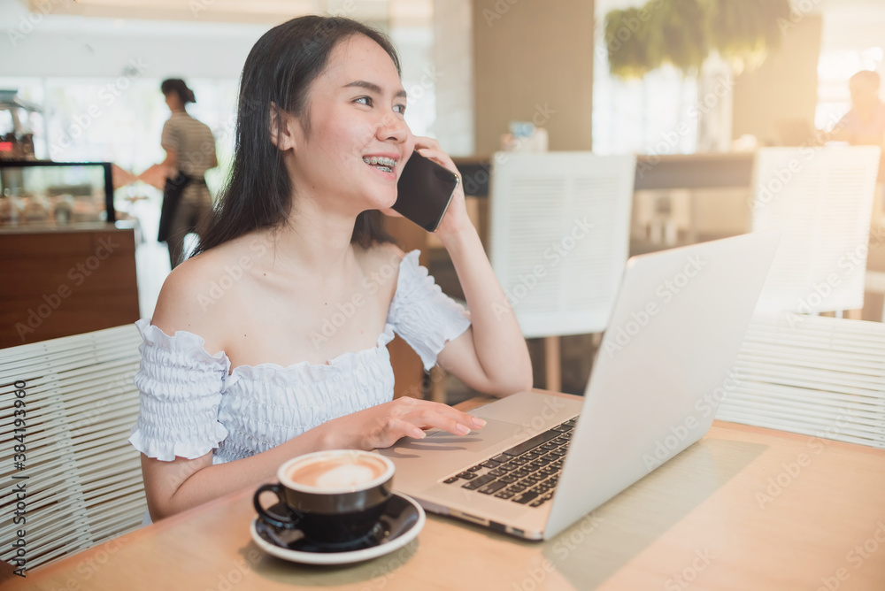 A woman sitting using a laptop and smartphone while eating coffee A woman sitting using a laptop and smartphone while eating coffee