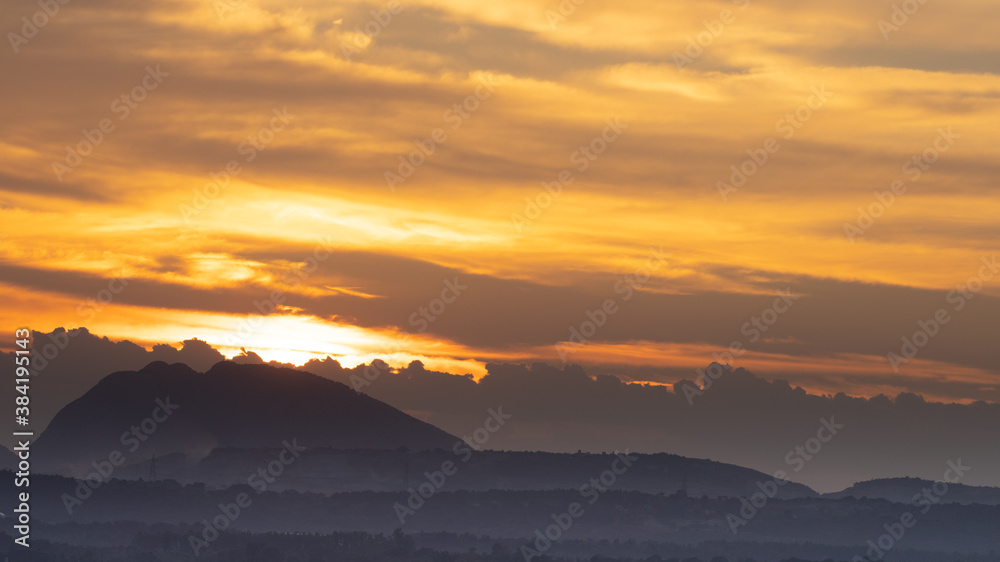 Silhouette of a hill against beautiful golden hour light and beautiful clouds formation in the horizon