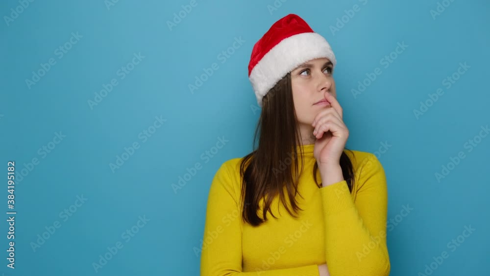 Dreamful cute woman think dream, and raising finger with great idea gesture, dressed in yellow cozy sweater and Christmas red hat, isolated on blue background. Happy New Year celebration merry holiday Dreamful cute woman think dream, and raising finger with great idea gesture, dressed in yellow cozy sweater and Christmas red hat, isolated on blue background. Happy New Year celebration merry holiday