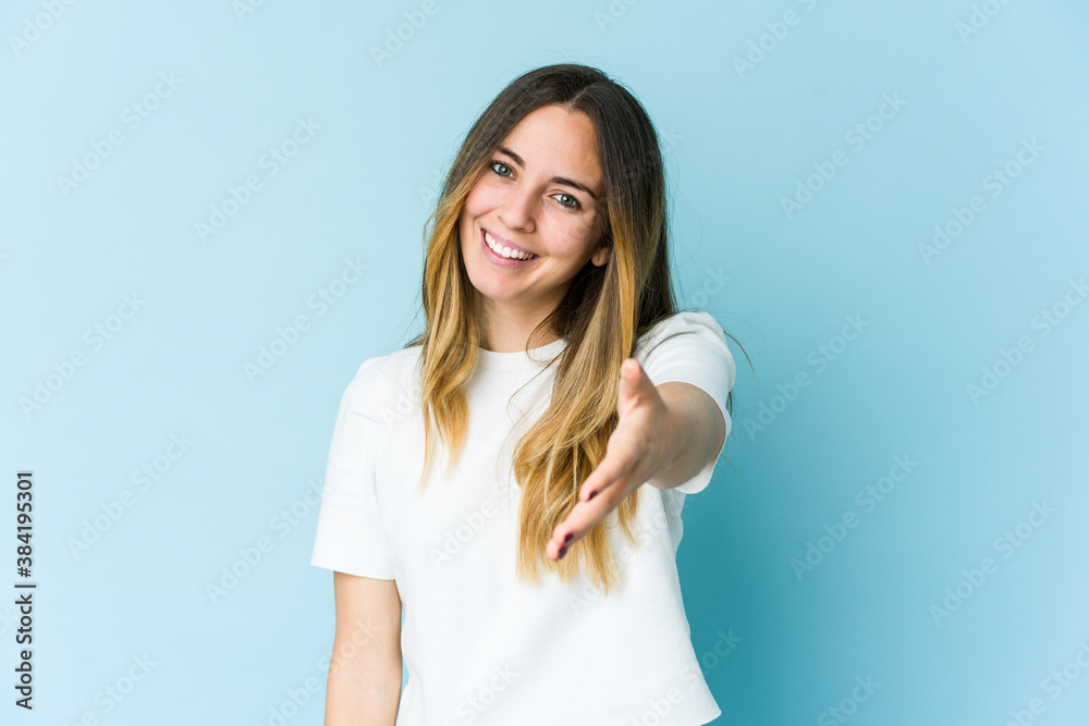 Young caucasian woman isolated on blue background stretching hand at camera in greeting gesture. Young caucasian woman isolated on blue background stretching hand at camera in greeting gesture.