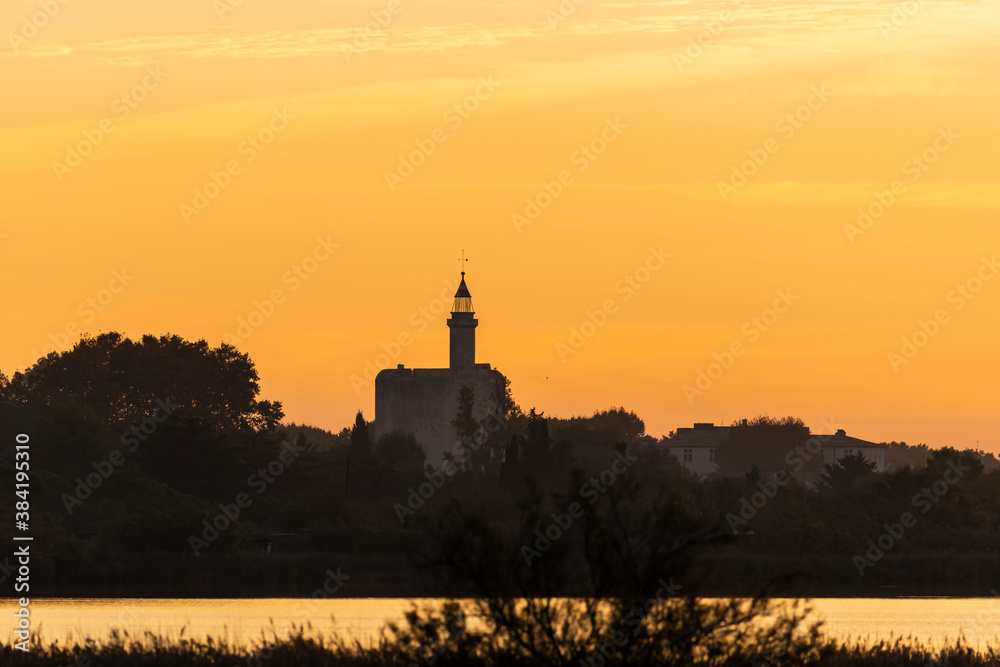 The Constance tower of the fortifications of the medieval city of Aigues-Mortes from the Marette pond at sunrise, in the Gard, in Occitanie, France