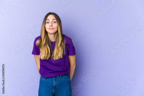 Young caucasian woman isolated on purple background shrugs shoulders and open eyes confused.