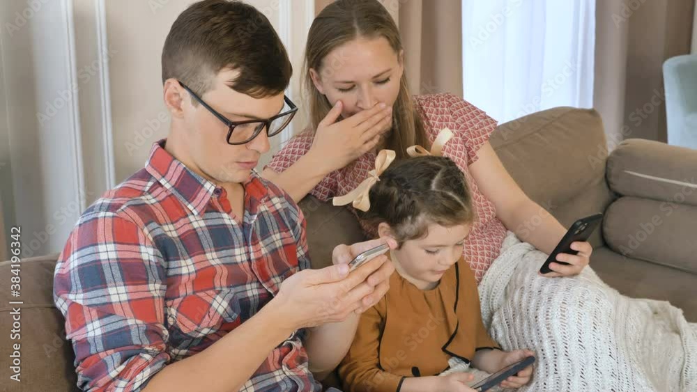 A young family sits at home with mobile phones and surf the Internet, make online purchases and chat with friends online A young family sits at home with mobile phones and surf the Internet, make online purchases and chat with friends online