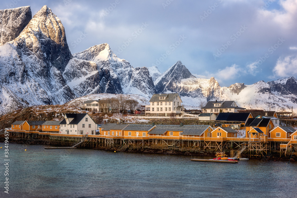 Traditional norwegian fishing houses rorbu on the Lofoten Islands, Hamnoy, Norway. Amazing winter landscape with snowy rocky mountains, water and blue sky with clouds, outdoor travel background