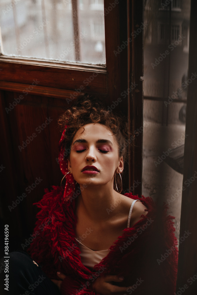 Beautiful girl in red woolen outfit sitting near wooden door Beautiful girl in red woolen outfit sitting near wooden door